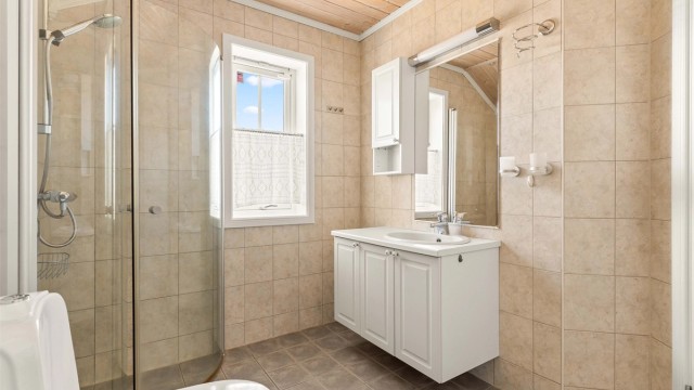 Badet er utstyrt med dusjnisje, gulvmontert toalett og servant med speil og overlys.