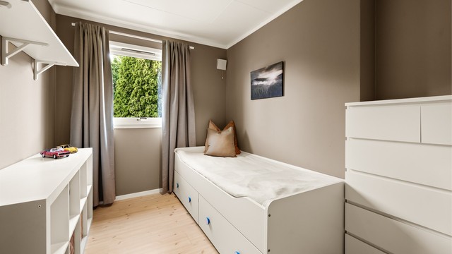 Lyst og trivelig soverom med plass til seng og oppbevaring.