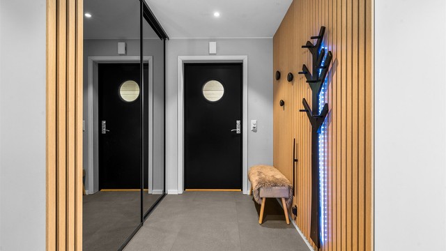Entreen har flislagte gulv med varme, spilevegger og moderne skyvedørsgarderobe med speilfronter i sort utførelse.