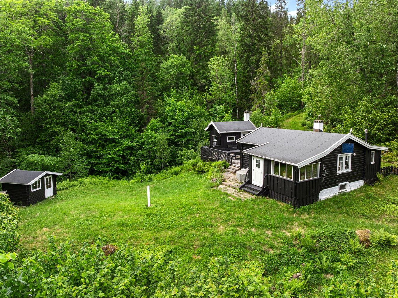 Tomten er omkranset av skog, med utsyn mot de grønne åssidene.