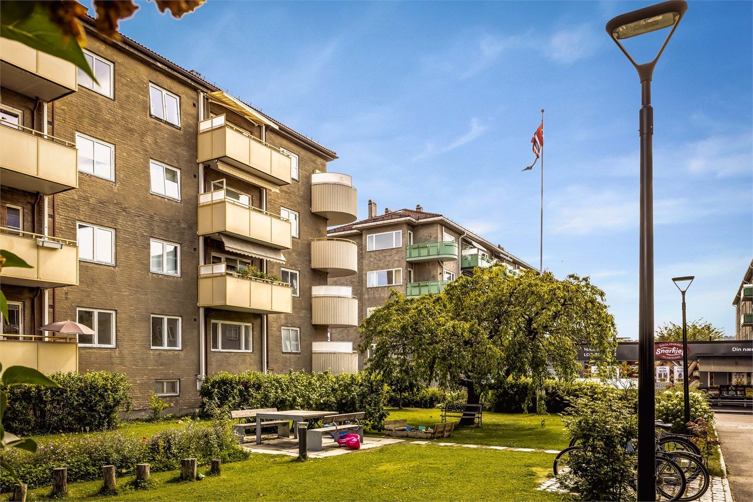 Fasade. Leiligheten vender i sin helhet mot bakgårdshagen. Fellesområdet er pent opparbeidet med gressplener, sittegrupper og lekeplass.