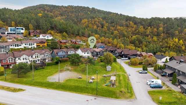 Dronebilde av eiendommen og nærområdet med fellesarealer og lekeplass i forkant av boligene