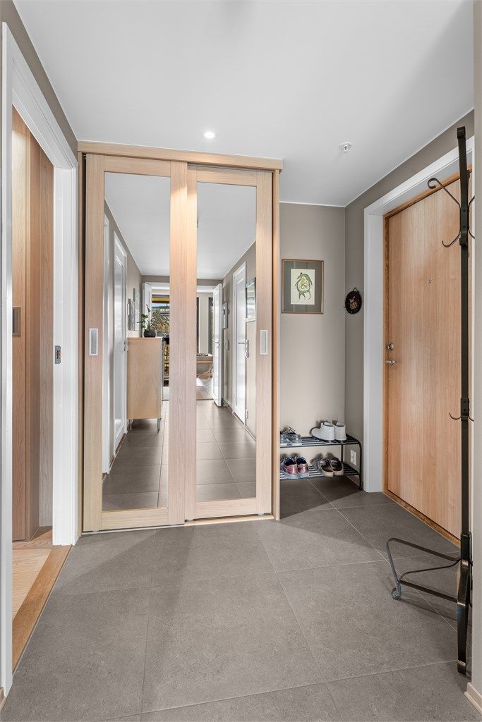 Pen entré med fliser på gulv og downlights i tak. Praktisk skyvedørsgarderobe for oppbevaring av yttertøy og sko. Gulvvarme
