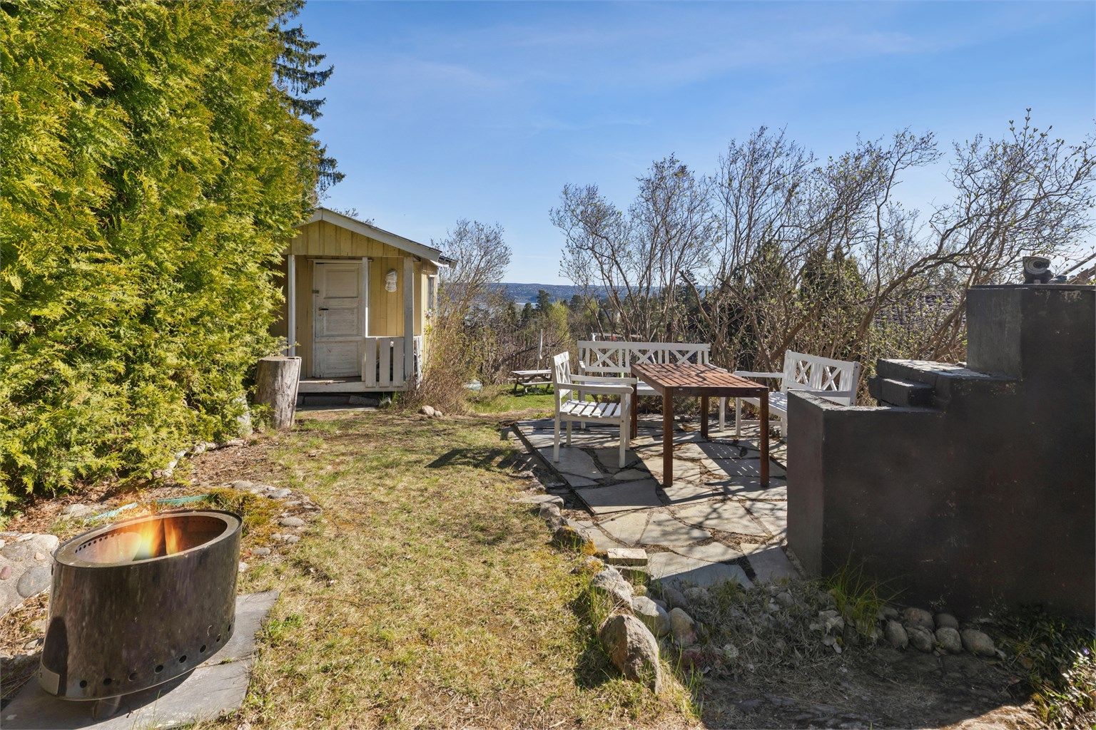 I hagen er det etablert en platting i skifer med utepeis, som skaper en svært hyggelig ramme for uteliv. Området har en idyllisk atmosfære, perfekt for sommerdager, barnelek og sosiale sammenkomster.