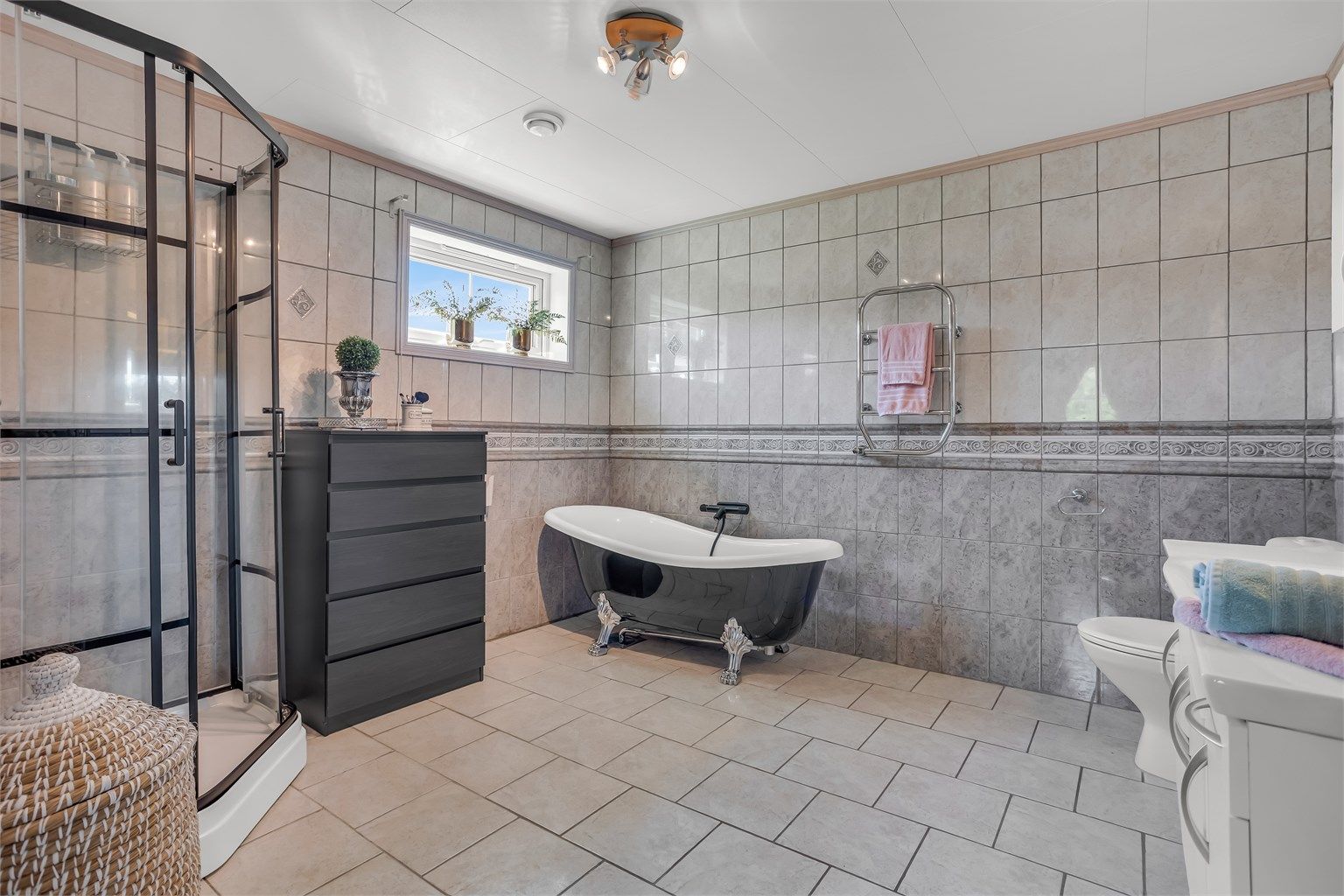 Badet er bestående av toalett, heldekkende servant i innredning, speil med belysning, badekar og dusjkabinett med skyvedører.