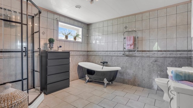 Badet er bestående av toalett, heldekkende servant i innredning, speil med belysning, badekar og dusjkabinett med skyvedører.