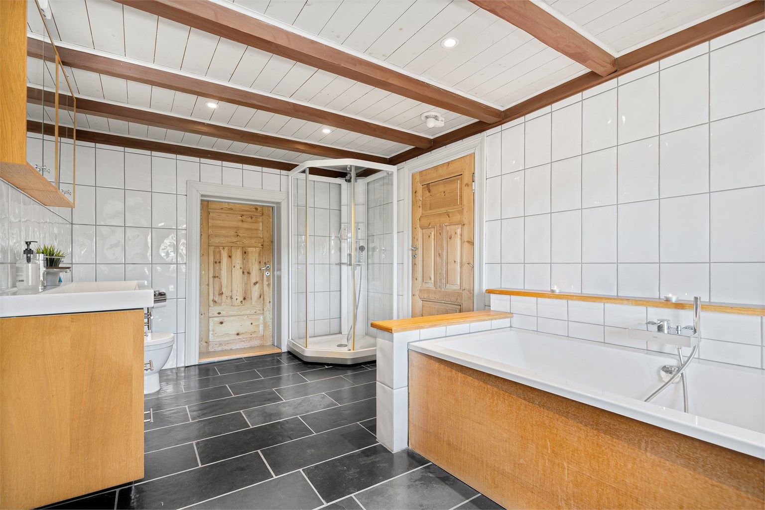 Badet i 2 etg. med varmekabler, badekar, dusjkabinett, wc, servant med skuffer og skap under og overskap. Inngang garderobe.