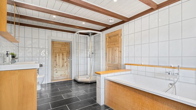 Badet i 2 etg. med varmekabler, badekar, dusjkabinett, wc, servant med skuffer og skap under og overskap. Inngang garderobe.