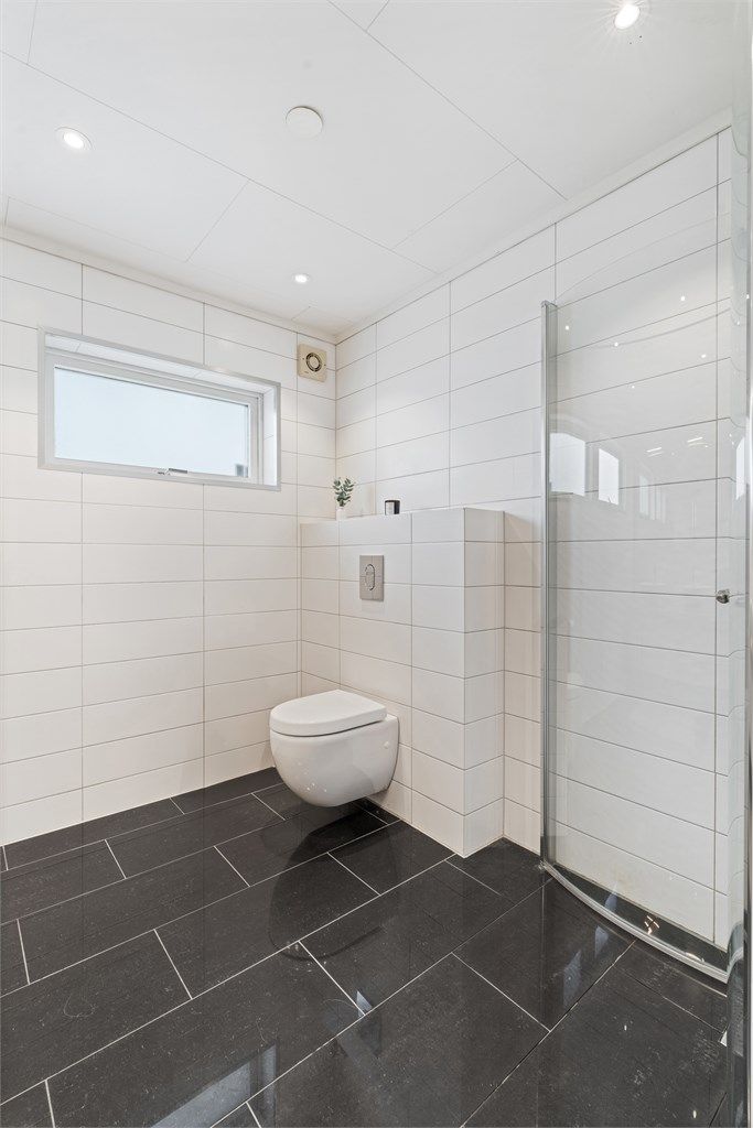 Badet har vegghengt toalett og dusjhjørne med dører.