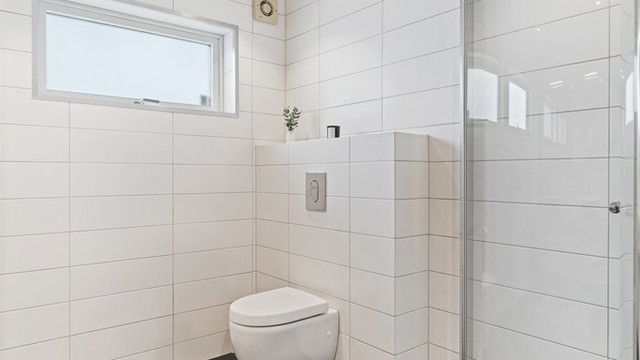 Badet har vegghengt toalett og dusjhjørne med dører.