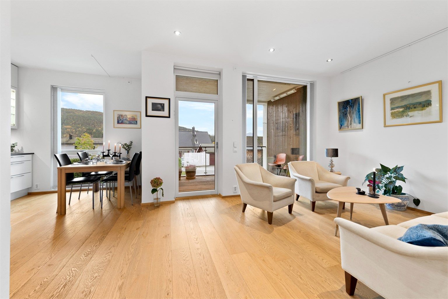 Stue og kjøkken i åpen løsning med lyse overflater og godt med naturlig lysinnslipp fra store vindusflater mot syd