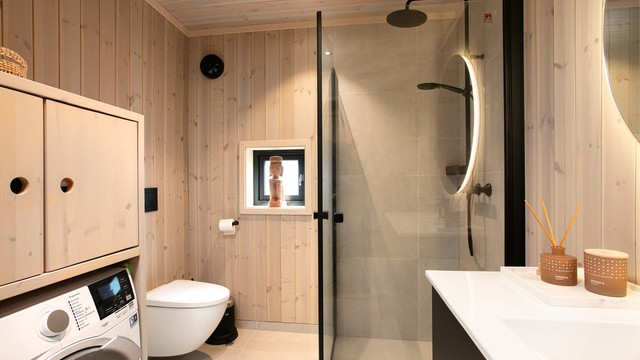 Badet er utstyrt med dusjhjørne med glassvegger og veggmontert toalett.
