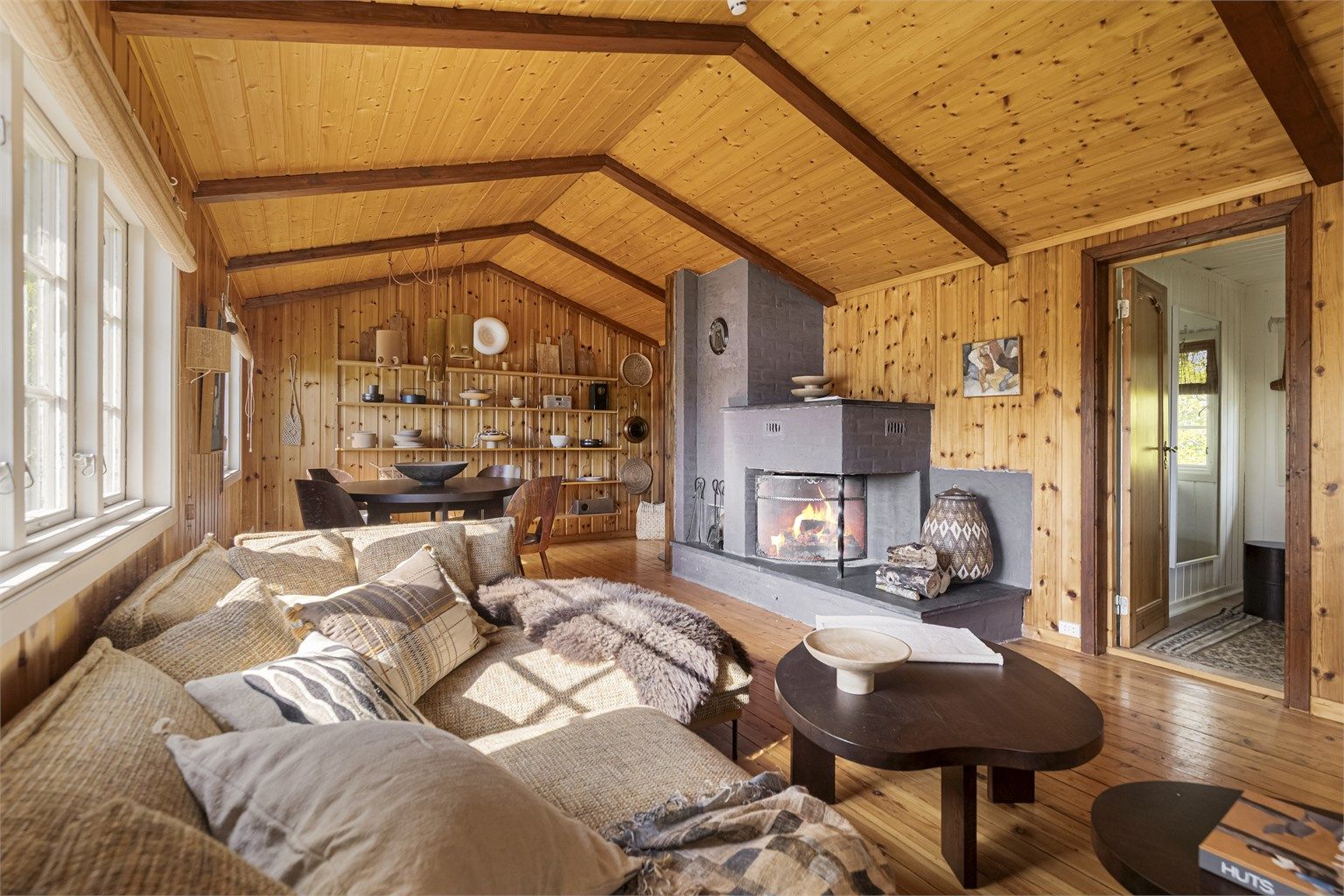 Stuen har rikelig med plass til både sofagruppe og spisebord. Den åpne peisen og vedovnen er perfekt for både varme og hygge på kalde dager.
