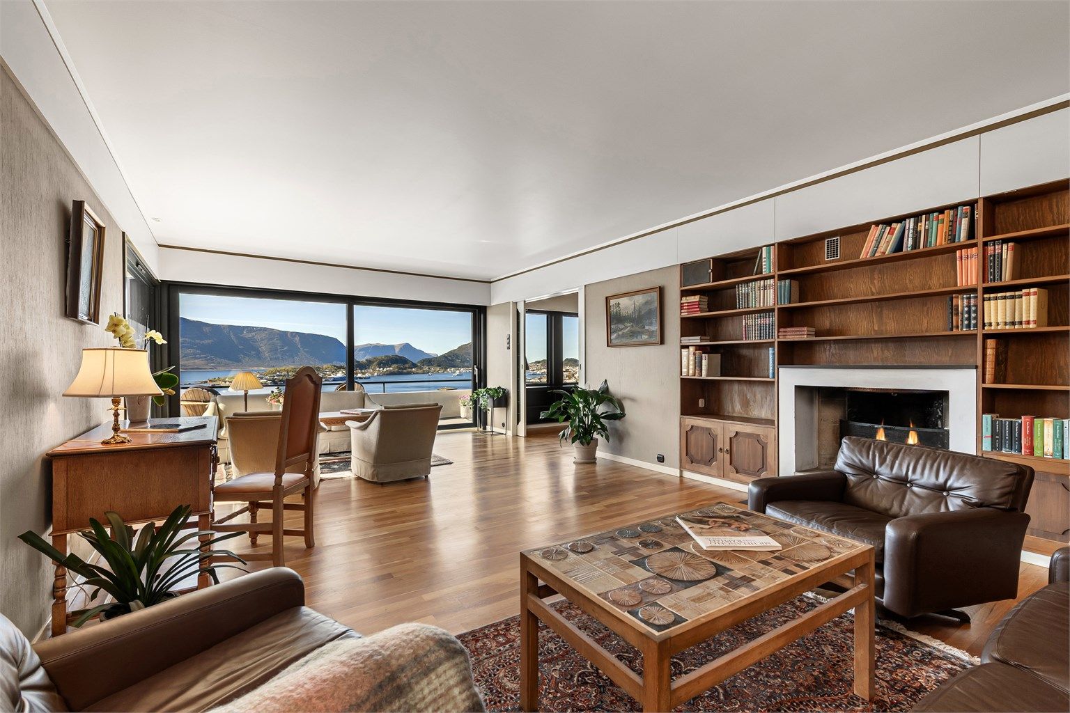 Stor stue med åpen peis og plassbygde reoler rundt. Store vindusflater med flott utsikt