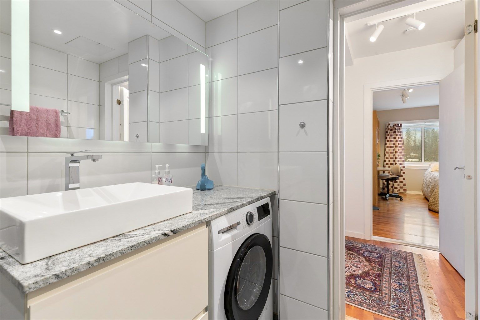 Innredningen består av et vegghengt servantskap, speil med belysning og opplegg for vaskemaskin.