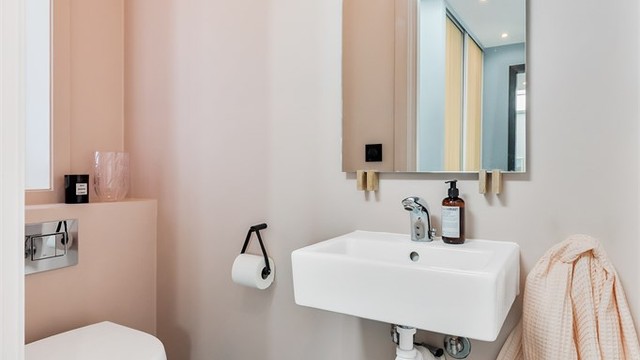 Toalettrom med flislagt gulv og vegger i malte flater. Nedsenket himling med downlights. Vegghengt servant med ett-greps armatur. Speil på vegg over servant. Vegghengt toalett. Mekanisk avtrekksventil i himling.