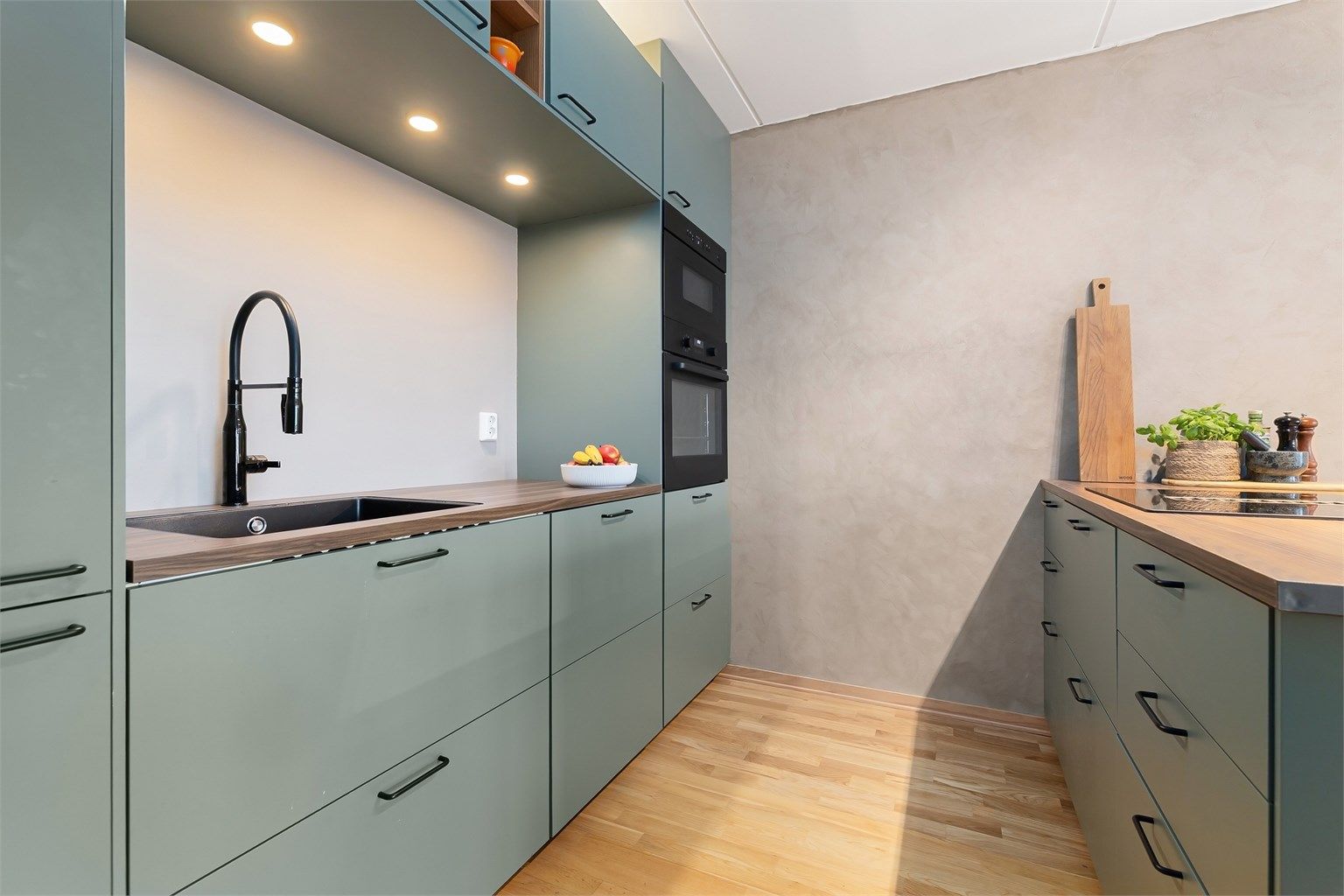 Innredning med grønne, glatte skapfronter, benkeplater i laminat, planlimt oppvaskkum og ett-greps armatur, begge i sort utførelse