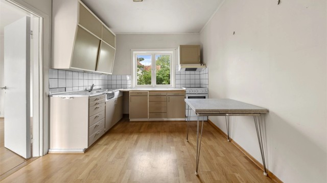Kjøkken med eldre innredning, glatte fronter og laminert benkeplate – med behov for modernisering og oppgradering.