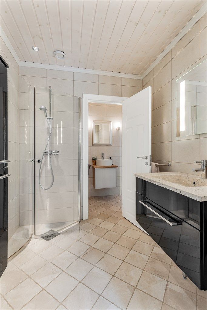 Baderom fra byggeår. Flislagt gulv med gulvvarme. Flislagte vegger. Vegghengt servantinnredning. Dusjhjørne med dører. Vegghengt dusjarmatur. Videre tilgang til toalettrommet.