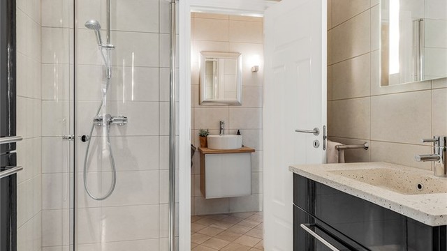 Baderom fra byggeår. Flislagt gulv med gulvvarme. Flislagte vegger. Vegghengt servantinnredning. Dusjhjørne med dører. Vegghengt dusjarmatur. Videre tilgang til toalettrommet.