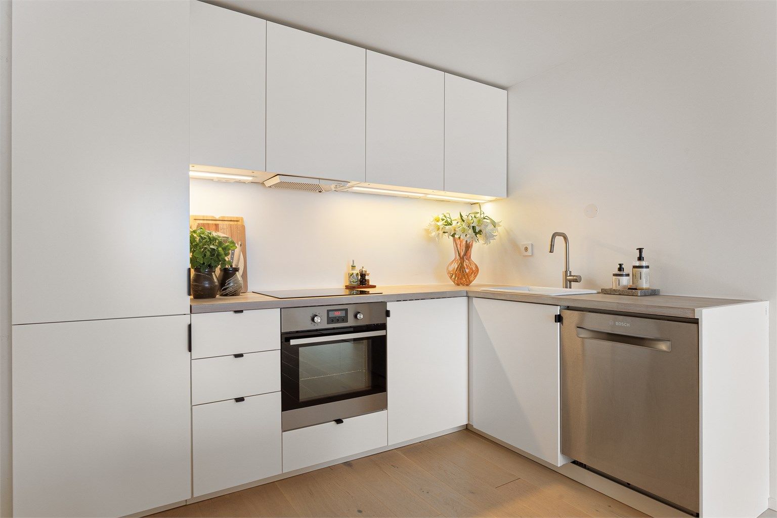 Lys køkkeninnredning med glatte fronter og laminatbenkeplate, med nedfelt vaskekum og integrert oppvaskmaskin.