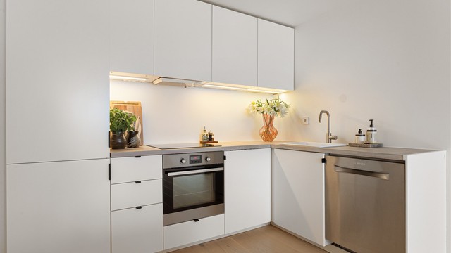 Lys køkkeninnredning med glatte fronter og laminatbenkeplate, med nedfelt vaskekum og integrert oppvaskmaskin.