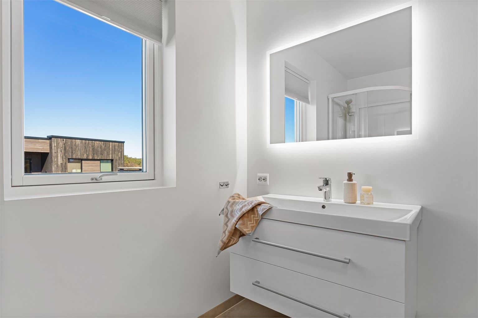 Stort vindu gir naturlig lys, ventilasjon, servant med oppbevaring og speil med lys som gir et moderne uttrykk