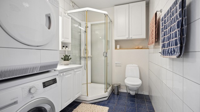 Lyst og delikat flislagt bad med behagelig gulvvarme som gir en lun start på dagen. Badet er innredet med servantskap, dusjkabinett og vegghengt toalett, samt praktisk plass for både vaskemaskin og tørketrommel.