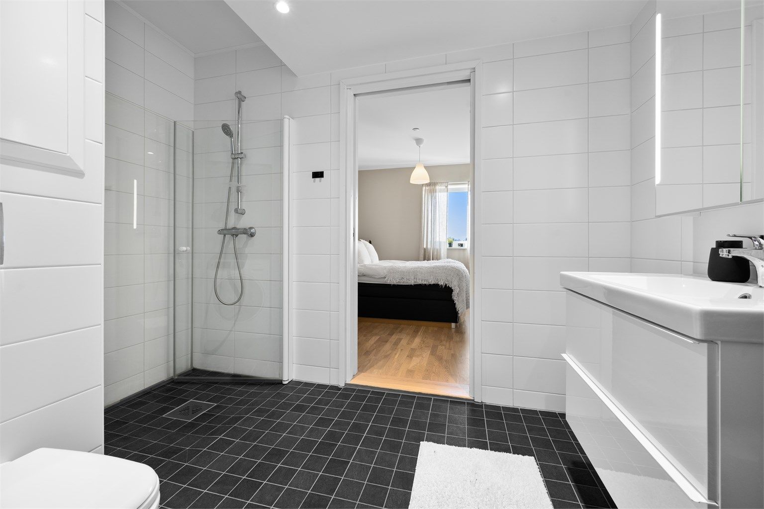 Dusjhjørne med innfellbare glassdører og veggmontert hånddusj. Vegghengt toalett med innebygget sisterne gir et stilrent og moderne uttrykk.