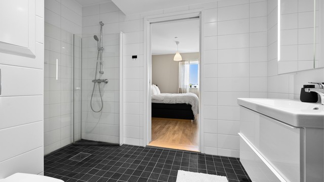 Dusjhjørne med innfellbare glassdører og veggmontert hånddusj. Vegghengt toalett med innebygget sisterne gir et stilrent og moderne uttrykk.