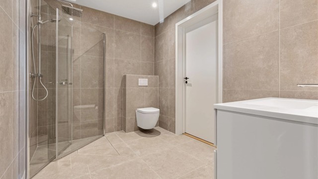 Badene er utstyrt med vegghengt toalett, servant og innfelte glassdører til dusj. Bad første etasje