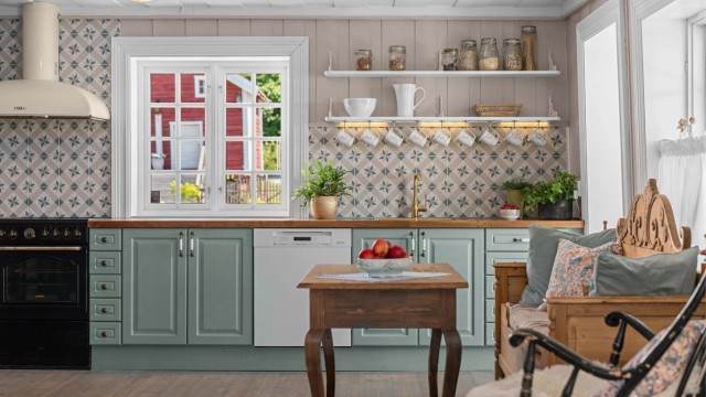 Kjøkkeninnredningen har profilerte fronter som er malt i farger som står i stil med andre deler av huset, og benkeplate av heltre med nedfelt oppvaskkum med ett-greps armatur