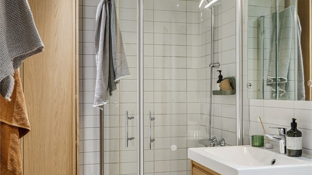 Badet er utstyrt med vegghengt toalett og dusjhjørne med innfellbare glassdører