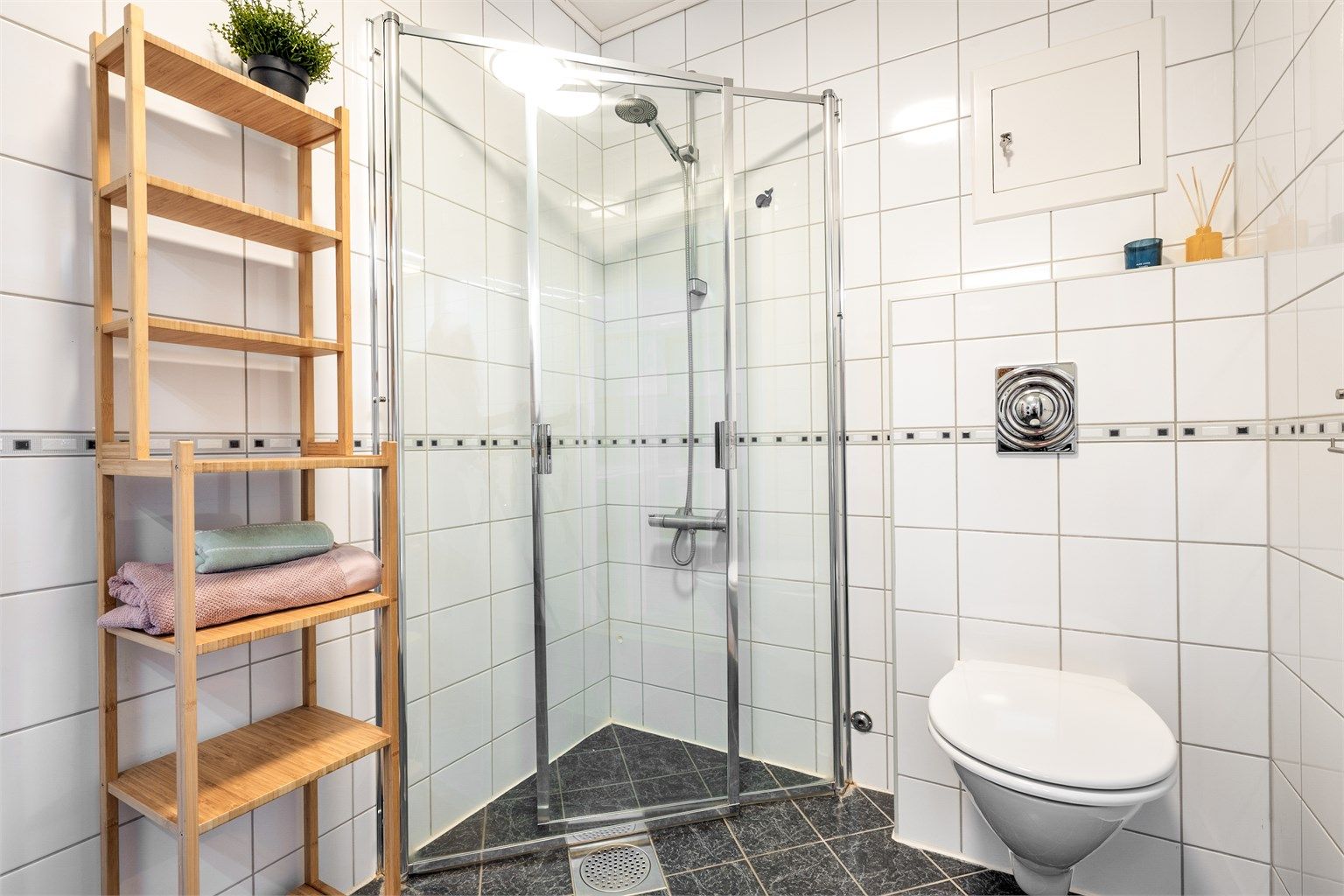 Badet er utstyrt med vegghengt toalett og et dusjhjørne med innfellbare glassdører.