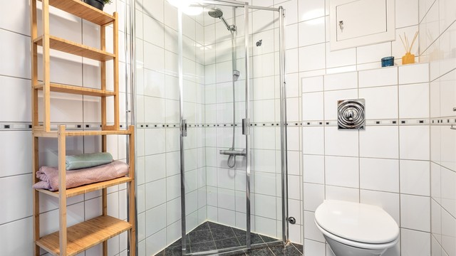 Badet er utstyrt med vegghengt toalett og et dusjhjørne med innfellbare glassdører.