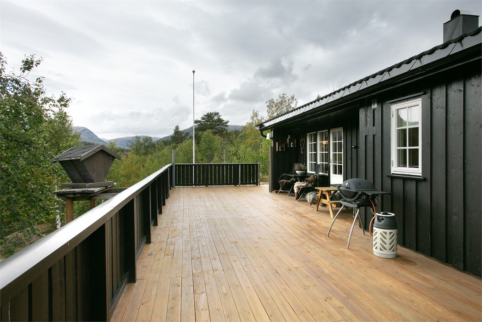 Langstrakt terrasse med rekkverk og god plass til utegrill og sittegrupper.