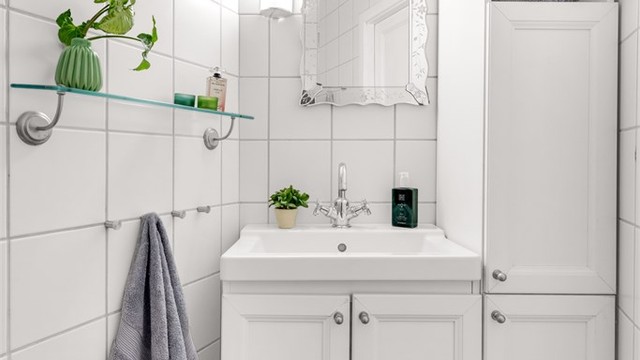 Badet er innredet med gulvstående servantinnredning med ovenpåliggende vask. Over vasken er det speil og lys. Det er også et gulvstående høyskap på badet som bidrar til ekstra oppbevaring.