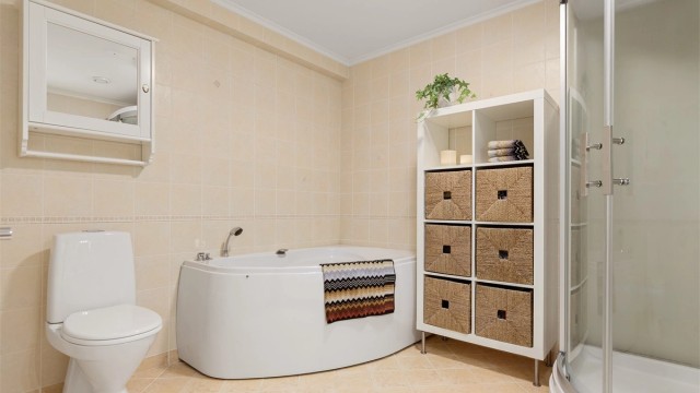 Lyst flislagt bad med gulvvarme i underetasje. Badet er innredet med badekar, steamdusj, gulvstående toalett og servantskap med speil og belysning