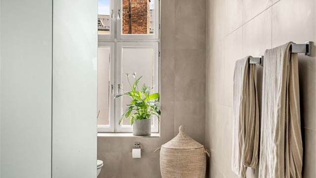 Badet er innredet med servantskap med ettgreps blandebatteri, vegghengt toalett med innebygget sisterne, speil med lys, avskjermet dusjhjørne med glass, blandebatteri og dusjgarnityr.