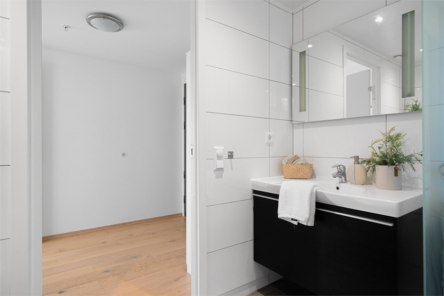 Stort speil på vegg. Det er mørke fliser på gulv og lyse på vegg. 