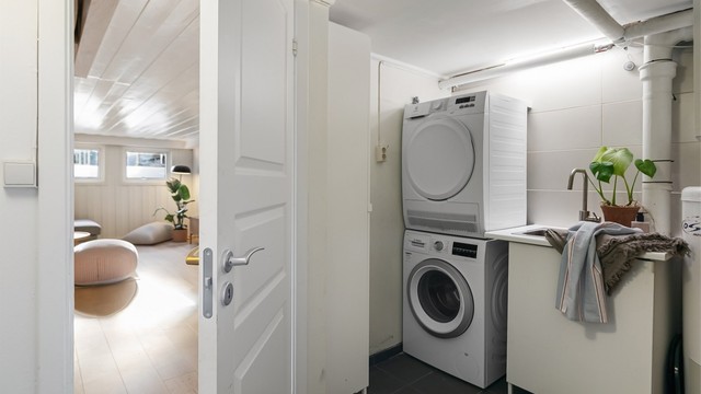 Separat vaskerom i kjeller med flislagt gulv, opplegg for vaskesøyle og utslagsvask.