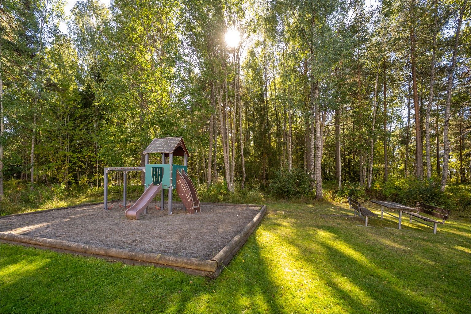 Skjermet fellesområde med lekeplass og benker like ved skogkanten.