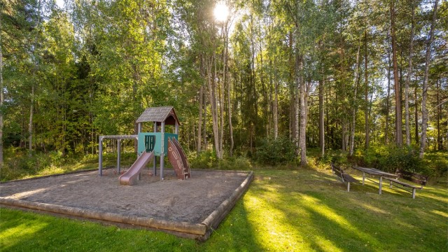 Skjermet fellesområde med lekeplass og benker like ved skogkanten.