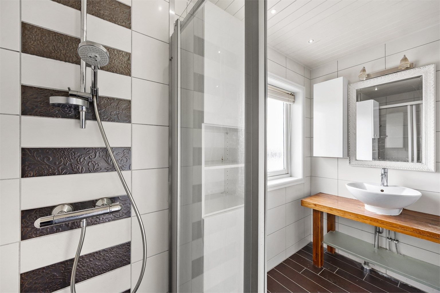 Dusjhjørne med skyvedør og dekorative detaljfliser.