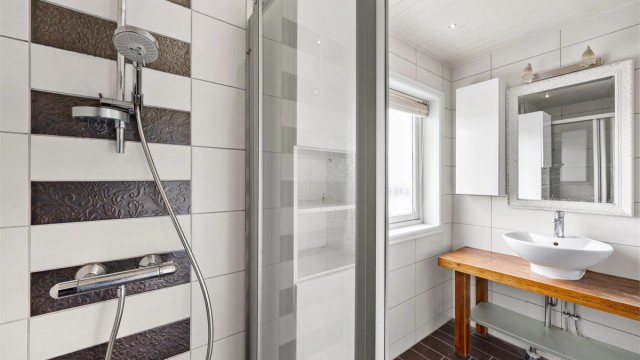 Dusjhjørne med skyvedør og dekorative detaljfliser.