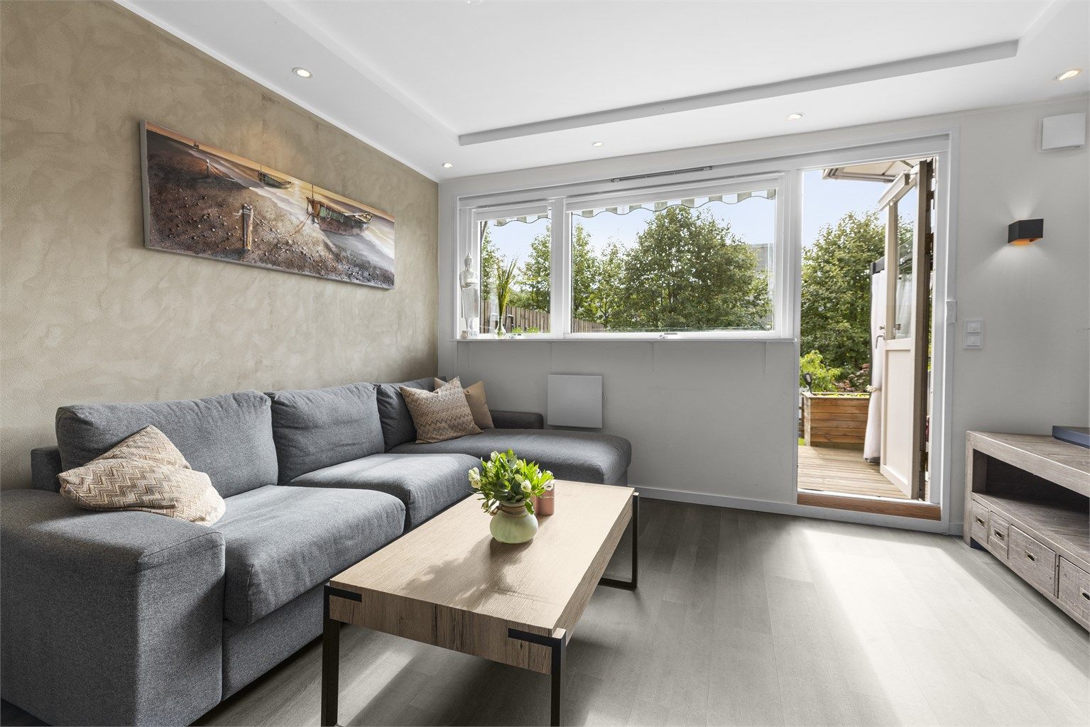 Romslig stue med plass for sofa, tilhørende salongbord, tv-seksjon og spisegruppe.