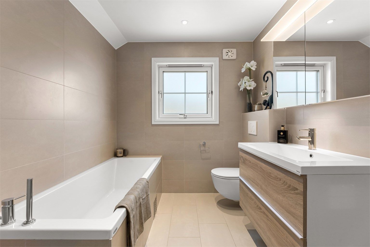 Pent baderom fra 2020 med fliser på gulv med gulvvarme, fliser på vegger og malt himling med downlights