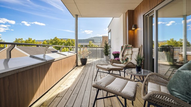 Balkong med utvendig belysning, terrassebord på gulv og rekkverk av metall samt glass.