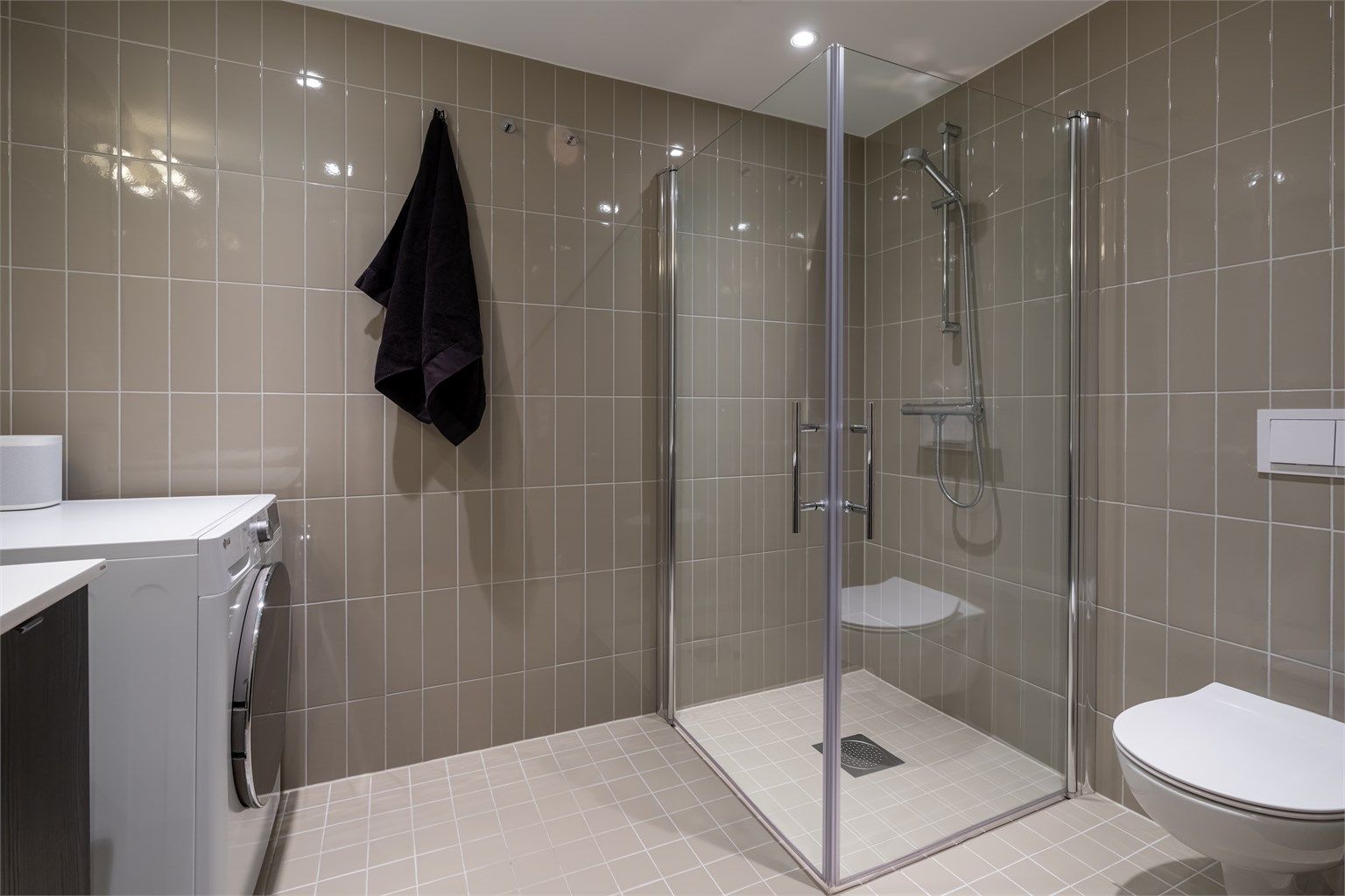 Videre er det vegghengt toalett og dusjhjørne med innfellbare glassdører. Baderommet har også opplegg for vaskemaskin og plass til tørketormmel.