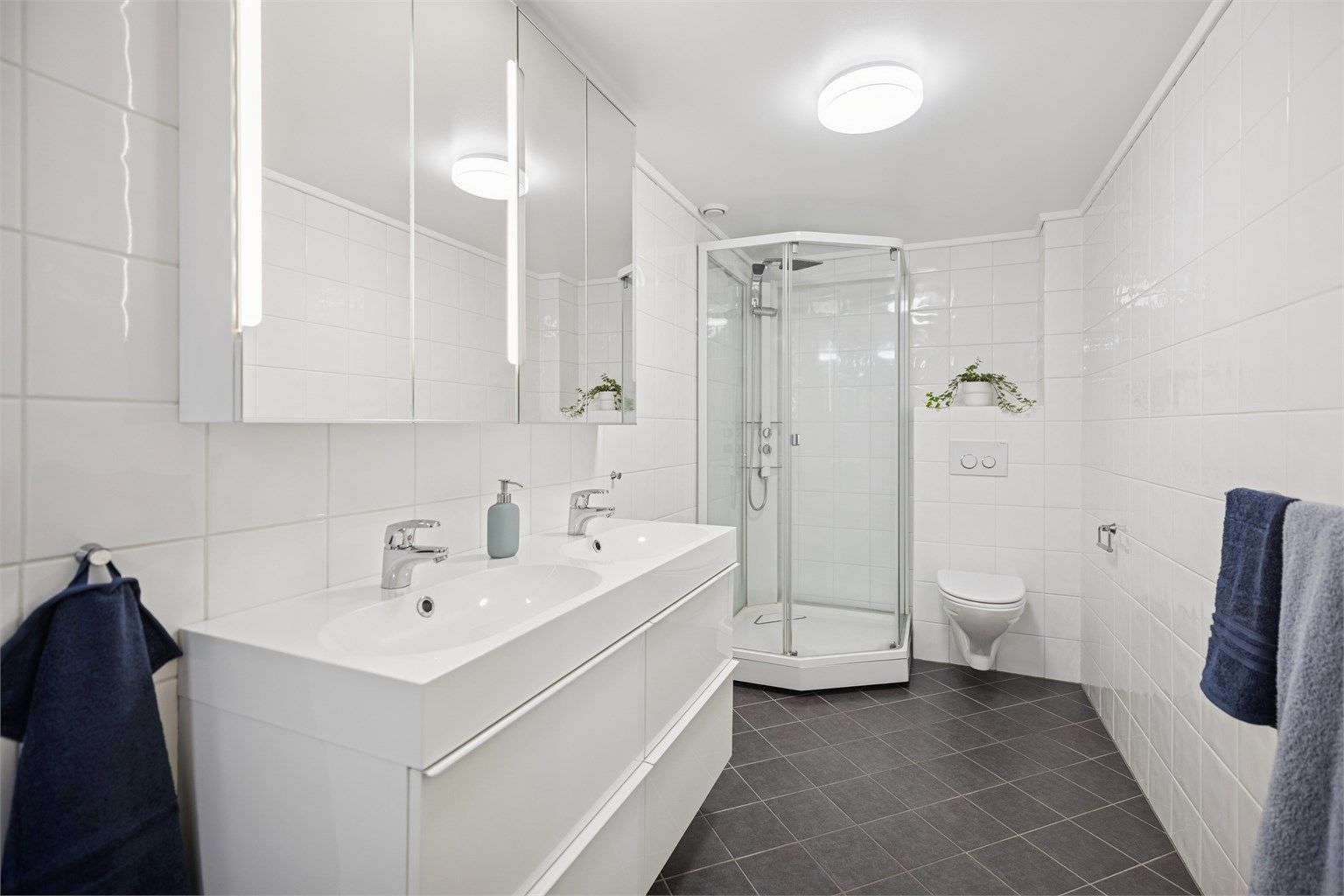 Pent flislagt bad/vaskerom i underetasjen med dobbel servantinnredning, dusjkabinett, vegghengt toalett og opplegg for vaskemaskin og tørketrommel.